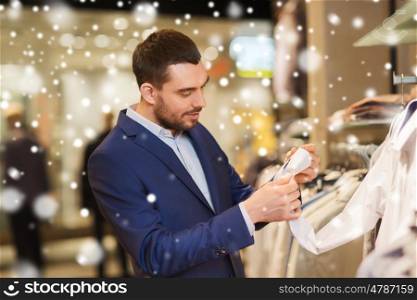 sale, shopping, fashion, style and people concept - elegant young man in suit choosing clothes in mall or clothing store over snow