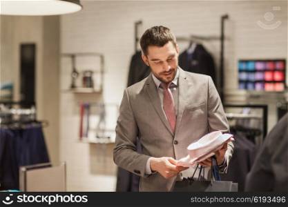 sale, shopping, fashion, style and people concept - elegant young man in suit choosing shirt in mall or clothing store