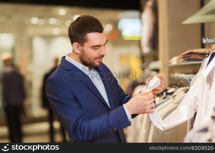 sale, shopping, fashion, style and people concept - elegant young man in suit choosing clothes in mall or clothing store