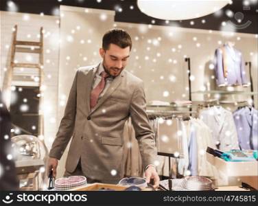 sale, shopping, fashion, style and people concept - happy elegant young man or businessman in suit choosing shirt in mall or clothing store over snow