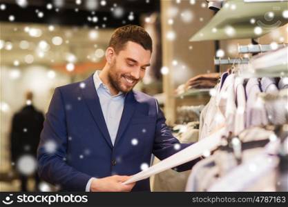 sale, shopping, fashion, style and people concept - happy elegant young man in suit choosing clothes in mall or clothing store over snow
