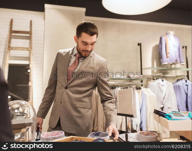sale, shopping, fashion, style and people concept - happy elegant young man or businessman in suit choosing shirt in mall or clothing store