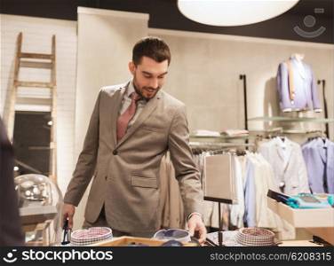 sale, shopping, fashion, style and people concept - happy elegant young man or businessman in suit choosing shirt in mall or clothing store