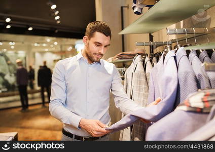 sale, shopping, fashion, style and people concept - happy young man in shirt choosing jacket in mall or clothing store