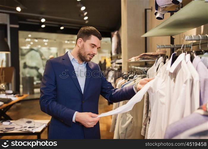 sale, shopping, fashion, style and people concept - happy young man in suit choosing shirt in mall or clothing store