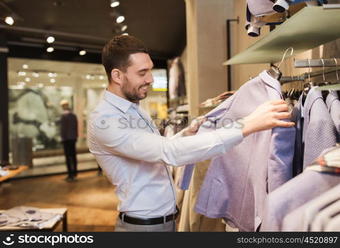 sale, shopping, fashion, style and people concept - happy young man in shirt choosing jacket in mall or clothing store