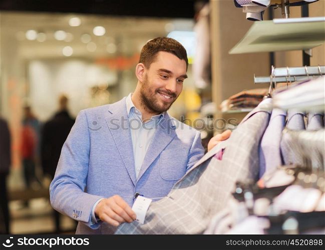 sale, shopping, fashion, style and people concept - happy young man in shirt choosing clothes in mall or clothing store