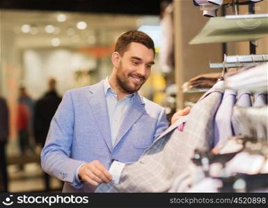 sale, shopping, fashion, style and people concept - happy young man in shirt choosing clothes in mall or clothing store