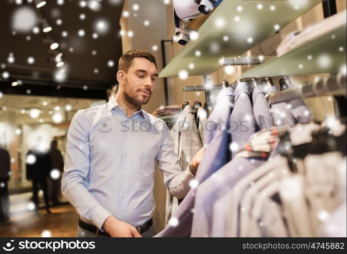 sale, shopping, fashion, style and people concept - happy young man in shirt choosing jacket in mall or clothing store over snow