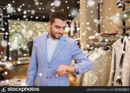 sale, shopping, fashion, style and people concept - happy young man in jacket looking at wristwatch at clothing store over snow