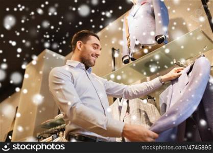 sale, shopping, fashion, style and people concept - happy young man in shirt choosing jacket in mall or clothing store over snow