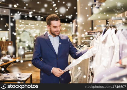 sale, shopping, fashion, style and people concept - happy young man in suit choosing shirt in mall or clothing store over snow