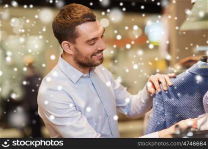 sale, shopping, fashion, style and people concept - happy young man in shirt choosing clothes in mall or clothing store over snow