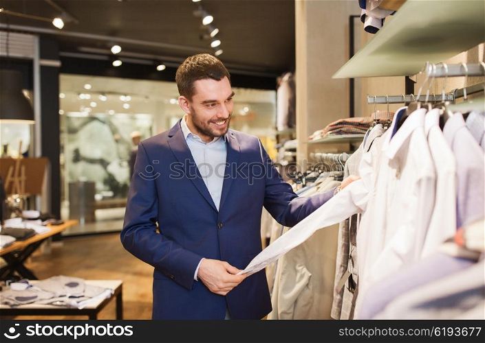 sale, shopping, fashion, style and people concept - happy young man in suit choosing shirt in mall or clothing store