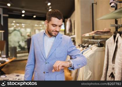 sale, shopping, fashion, style and people concept - happy young man in jacket looking at wristwatch at clothing store