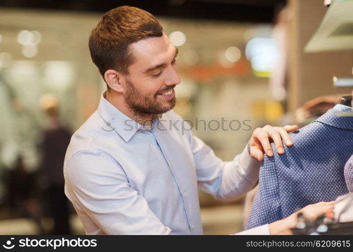 sale, shopping, fashion, style and people concept - happy young man in shirt choosing clothes in mall or clothing store