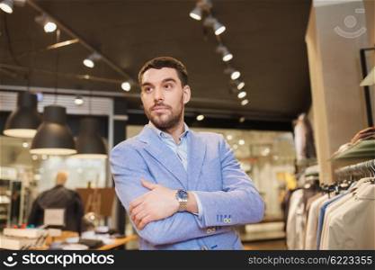 sale, shopping, fashion, style and people concept - happy young man or businessman in jacket and wristwatch at clothing store