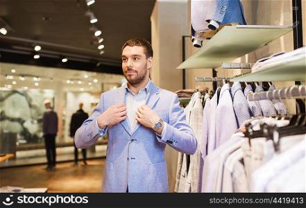sale, shopping, fashion, style and people concept - happy young man trying suit at clothing store