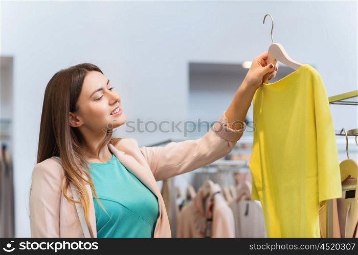 sale, shopping, fashion, style and people concept - happy young woman choosing clothes in mall or clothing store