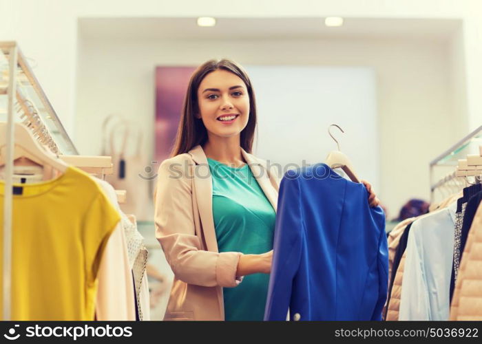 sale, shopping, fashion, style and people concept - happy young woman choosing clothes in mall or clothing store. happy young woman choosing clothes in mall