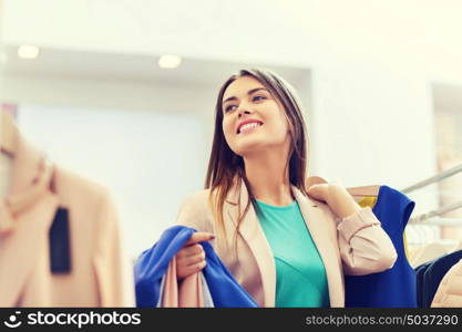 sale, shopping, fashion, style and people concept - happy young woman choosing clothes in mall or clothing store. happy young woman choosing clothes in mall