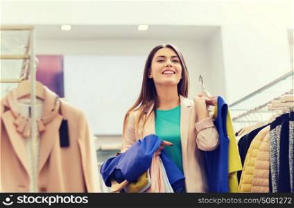 sale, shopping, fashion, style and people concept - happy young woman choosing clothes in mall or clothing store. happy young woman choosing clothes in mall
