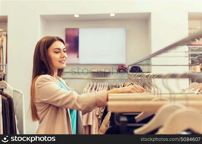 sale, shopping, fashion, style and people concept - happy young woman choosing clothes in mall or clothing store. happy young woman choosing clothes in mall. happy young woman choosing clothes in mall