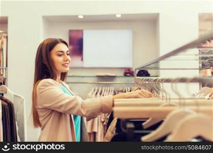 sale, shopping, fashion, style and people concept - happy young woman choosing clothes in mall or clothing store. happy young woman choosing clothes in mall. happy young woman choosing clothes in mall