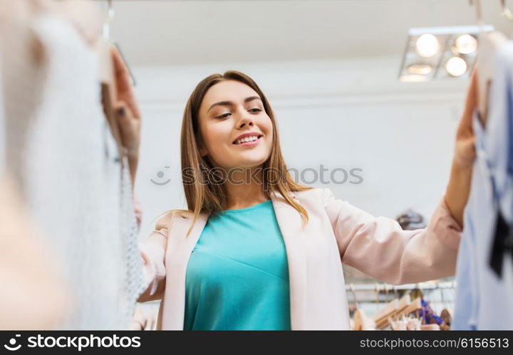 sale, shopping, fashion, style and people concept - happy young woman choosing clothes in mall or clothing store