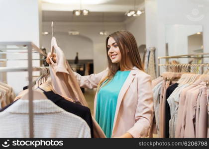 sale, shopping, fashion, style and people concept - happy young woman choosing clothes in mall or clothing store