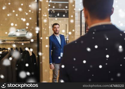 sale, shopping, fashion, style and people concept - young man choosing and trying jacket on and looking to mirror in mall or clothing store over snow