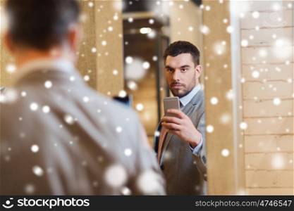 sale, shopping, fashion, style and people concept - young man in suit with smartphone taking mirror selfie at clothing store over snow