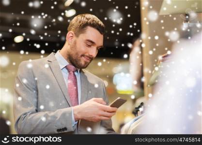 sale, shopping, fashion, technology and people concept - happy man in suit with smartphone choosing clothes at clothing store over snow