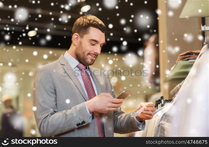 sale, shopping, fashion, technology and people concept - happy man in suit with smartphone choosing clothes at clothing store over snow