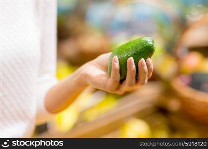sale, shopping, food, consumerism and people concept - close up of woman hand holding avocado in market