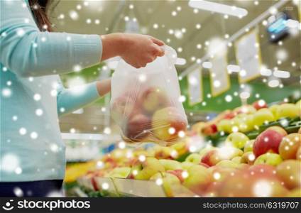 sale, shopping, food, consumerism and people concept - female customer holding bag with apples at grocery store over snow. woman with bag buying apples at grocery store