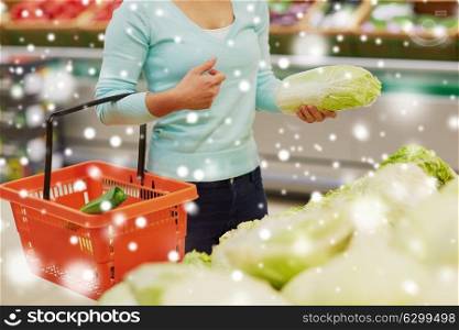 sale, shopping, food, consumerism and people concept - female customer with basket buying chinese cabbage at grocery store over snow. woman with basket and chinese cabbage at grocery