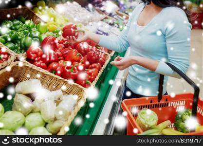 sale, shopping, food, consumerism and people concept - female customer with basket buying bell peppers or paprika at grocery store over snow. customer buying peppers at grocery store