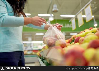 sale, shopping, food, consumerism and people concept - woman tying bag with apples at grocery store. woman with bag buying apples at grocery store