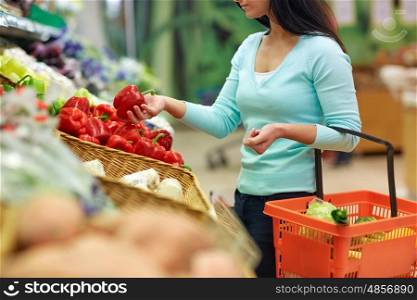 sale, shopping, food, consumerism and people concept - woman with basket buying bell peppers or paprika at grocery store