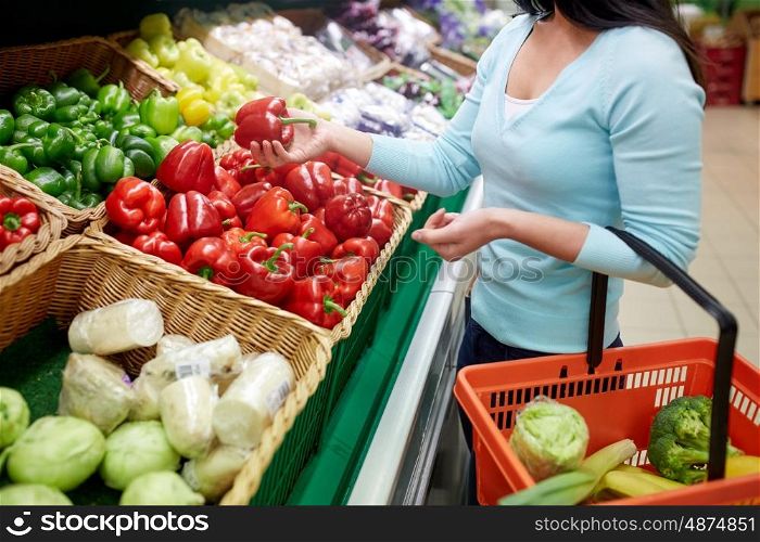 sale, shopping, food, consumerism and people concept - woman with basket buying bell peppers or paprika at grocery store