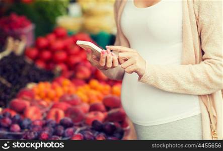 sale, shopping, food, pregnancy and people concept - close up of pregnant woman with smartphone at street market