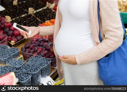 sale, shopping, food, pregnancy and people concept - close up of pregnant woman with smartphone and shopper bag at street market