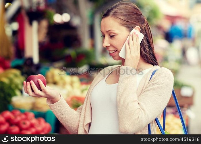 sale, shopping, food, pregnancy and people concept - happy pregnant woman choosing fruits and calling on smartphone at street market