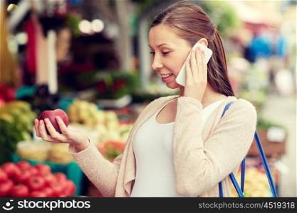 sale, shopping, food, pregnancy and people concept - happy pregnant woman choosing fruits and calling on smartphone at street market
