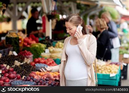 sale, shopping, food, pregnancy and people concept - happy pregnant woman choosing berries and calling on smartphone at street market
