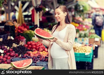 sale, shopping, food, pregnancy and people concept - happy pregnant woman choosing watermelon at street market