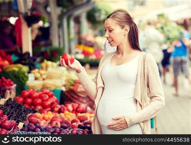sale, shopping, food, pregnancy and people concept - happy pregnant woman holding tomato at street market