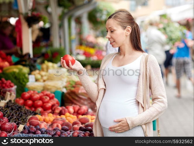 sale, shopping, food, pregnancy and people concept - happy pregnant woman holding tomato at street market