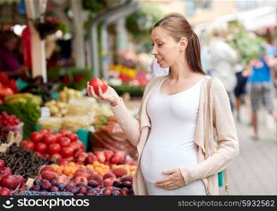 sale, shopping, food, pregnancy and people concept - happy pregnant woman holding tomato at street market